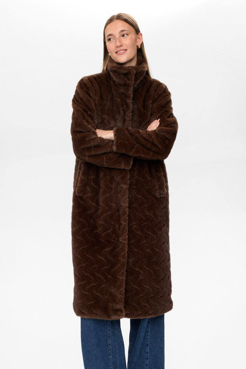 Woman wearing a long brown fur coat on a white background