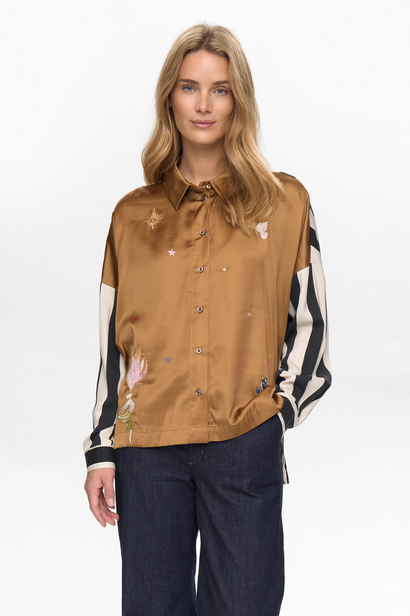 Woman wearing a brown shirt with floral patterns and dark pants on a white background