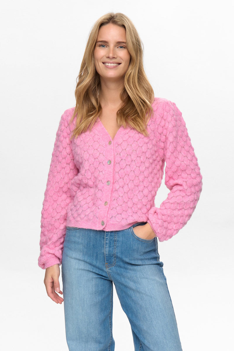 Woman wearing a pink textured cardigan and blue jeans on a white background