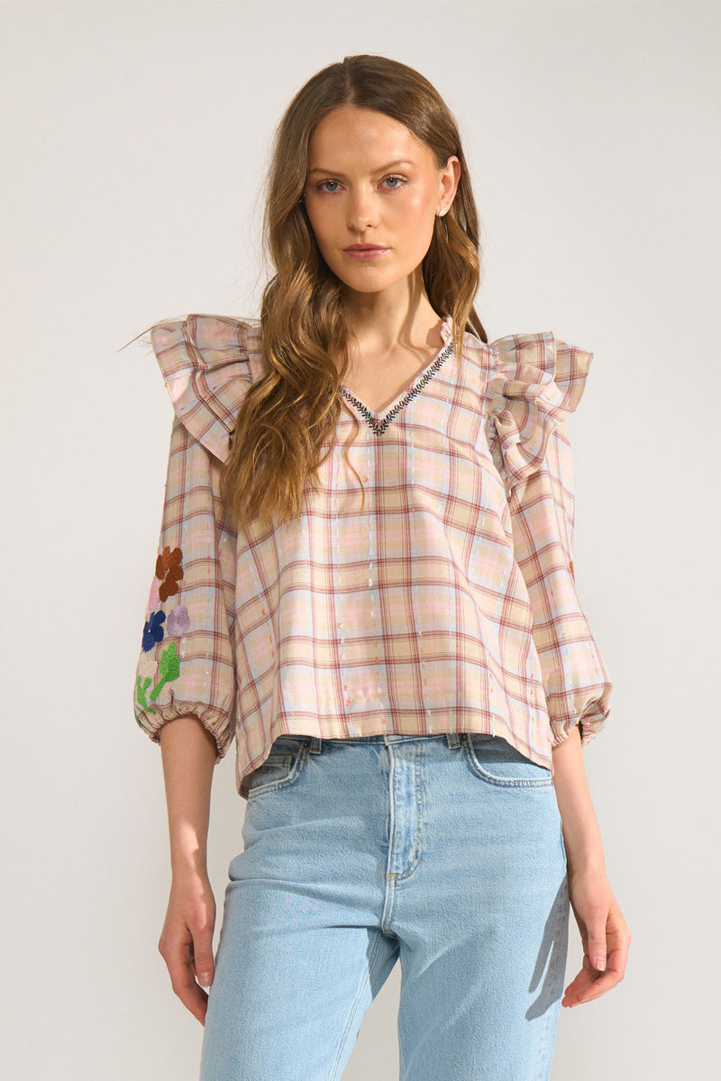 Woman wearing a plaid blouse with floral embroidery and light blue jeans on a white background