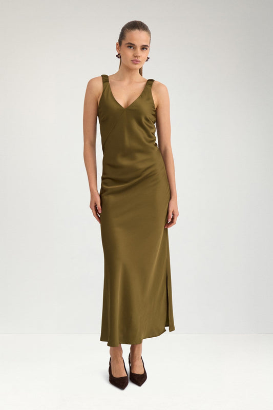 A woman modeling a sleeveless olive green satin midi dress with a V-neckline and side slit, paired with dark brown pointed-toe heels, against a plain light gray studio background.