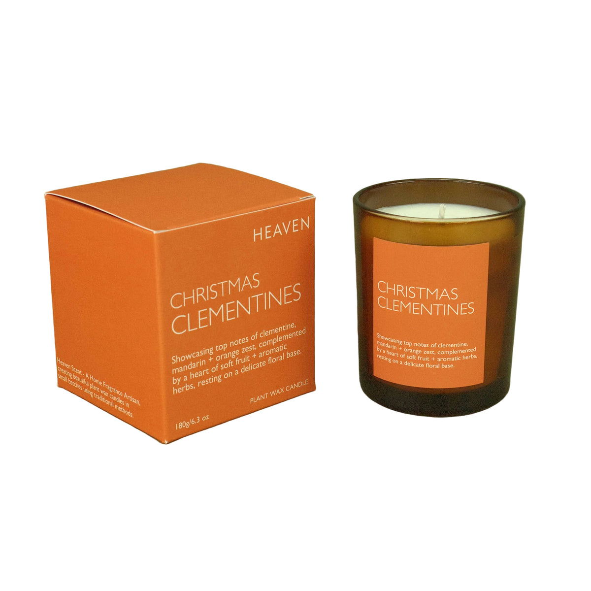 An amber glass jar candle and its matching orange box on a solid olive green background. The product is labeled 'Heaven Christmas Clementines'.