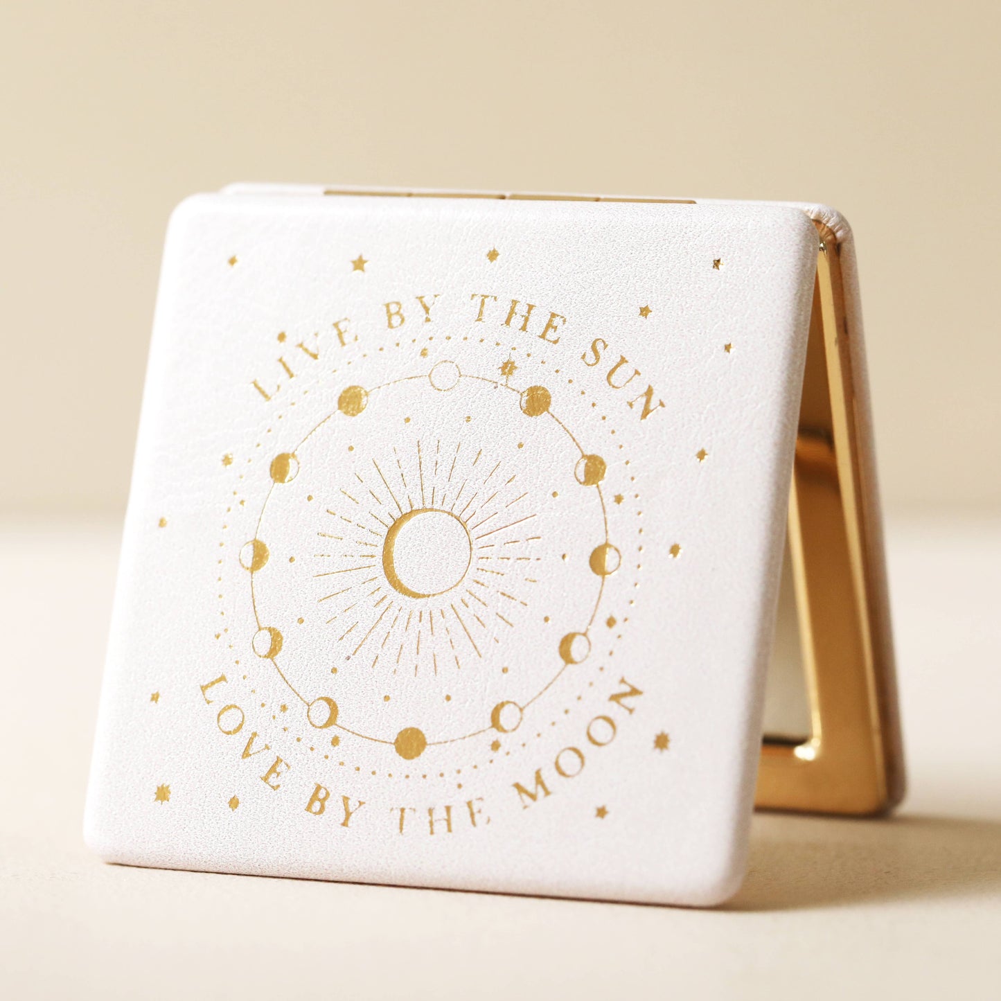 Compact mirror with gold text and celestial design on a beige background