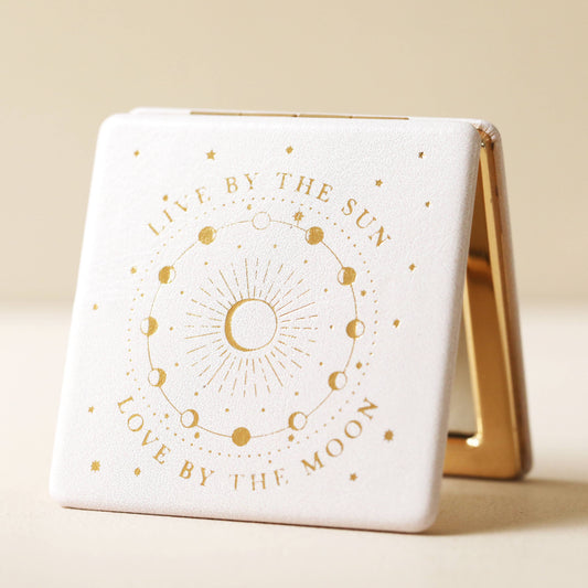 Compact mirror with gold text and celestial design on a beige background