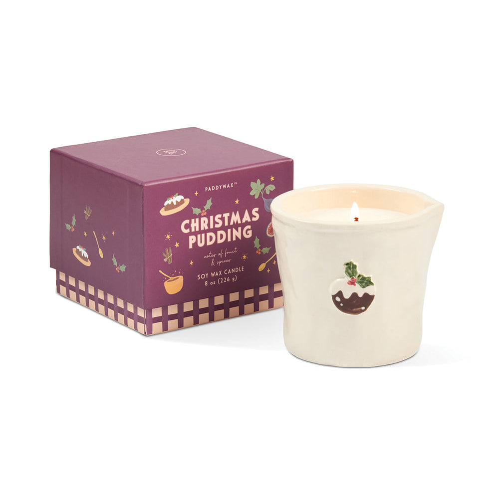 A FirstFragrance 'Christmas Pudding' scented soy wax candle next to its dark purple packaging box, set against a plain white background.
