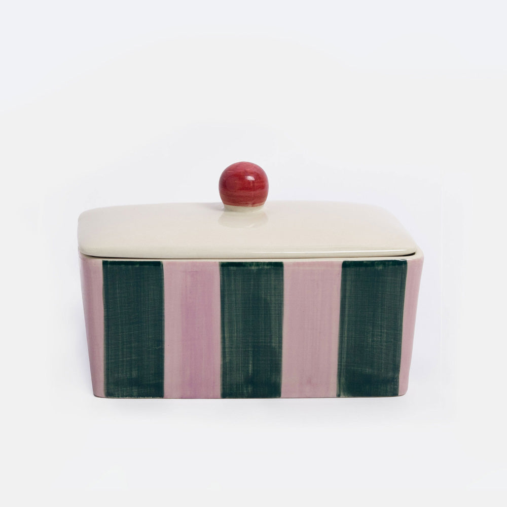 A rectangular lidded ceramic container with a cream-colored top and lid, featuring vertical stripes in dusty pink and dark green on the sides, topped with a small round red knob, set against a plain white background.