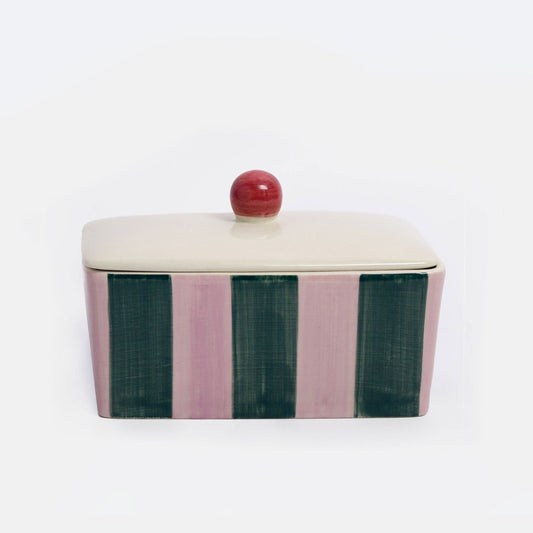 A rectangular lidded ceramic container with a cream-colored top and lid, featuring vertical stripes in dusty pink and dark green on the sides, topped with a small round red knob, set against a plain white background.