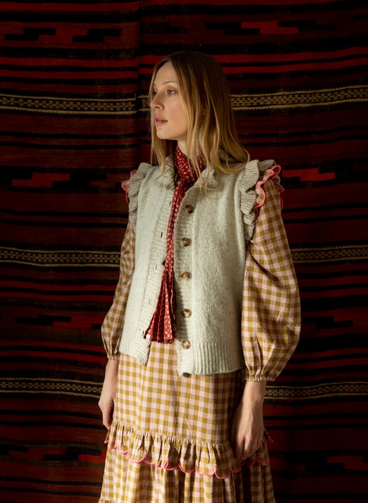 Woman wearing a checkered dress with a ruffled vest against a patterned wall.
