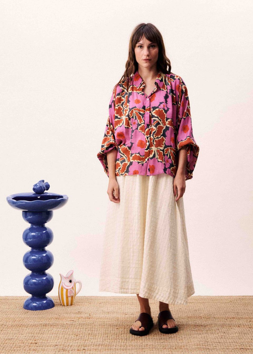 Woman wearing a colorful floral blouse and white pants standing in front of a blue decorative object.