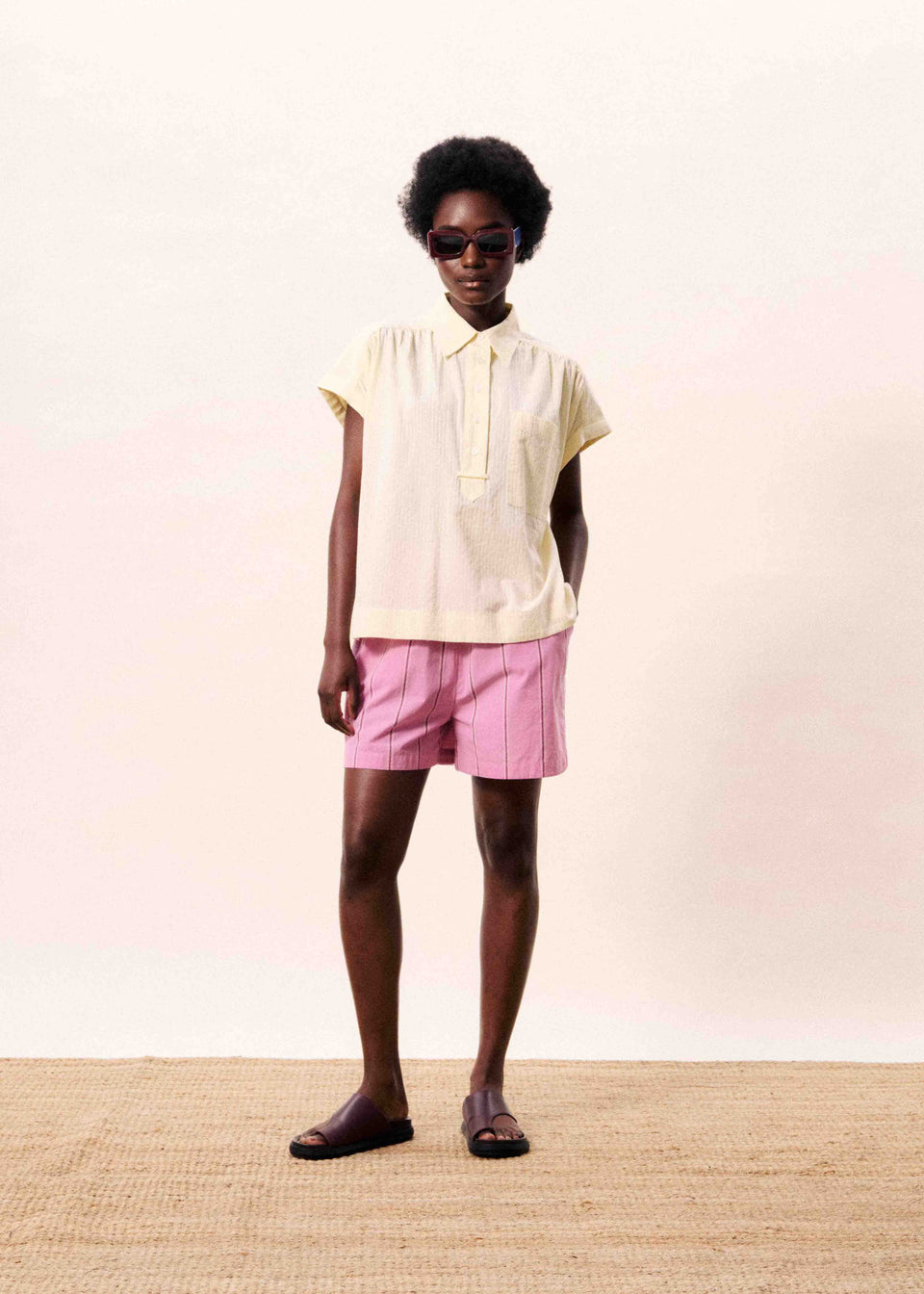 Person wearing a light yellow polo shirt and pink shorts on a plain background