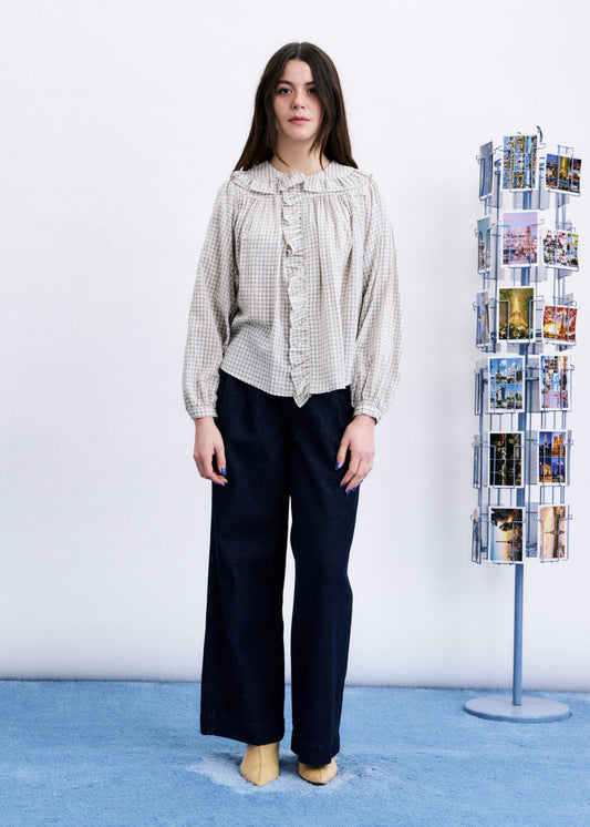 Woman wearing a checkered blouse and dark pants standing next to a magazine rack with brochures on a blue floor.