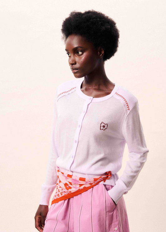 Woman wearing a pale pink long-sleeve shirt with red accents and pink pants on a beige background