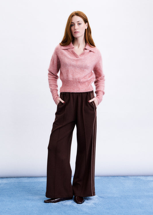 Woman wearing a pink sweater and brown pants on a white background