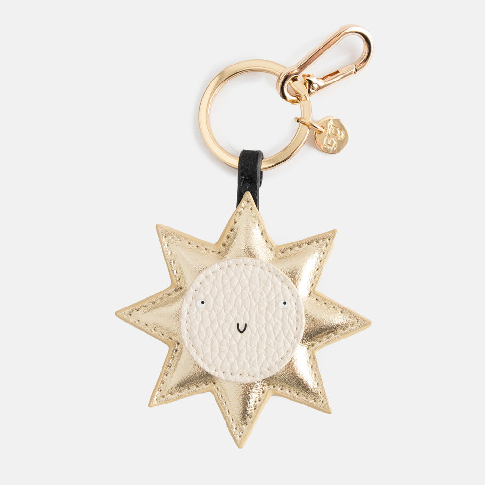 Caroline Gardner Gold Smiling Sun Bag Charm. Gold star-shaped keychain with a white ball centre on a white background