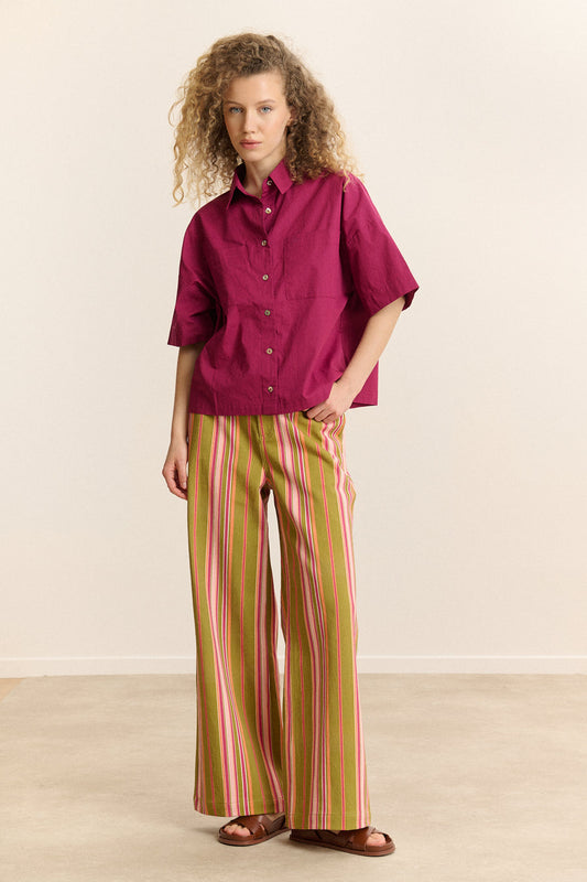 Woman wearing a magenta shirt and striped pants standing against a plain background