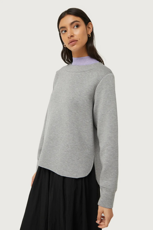 Woman wearing a gray sweater over a black skirt on a white background
