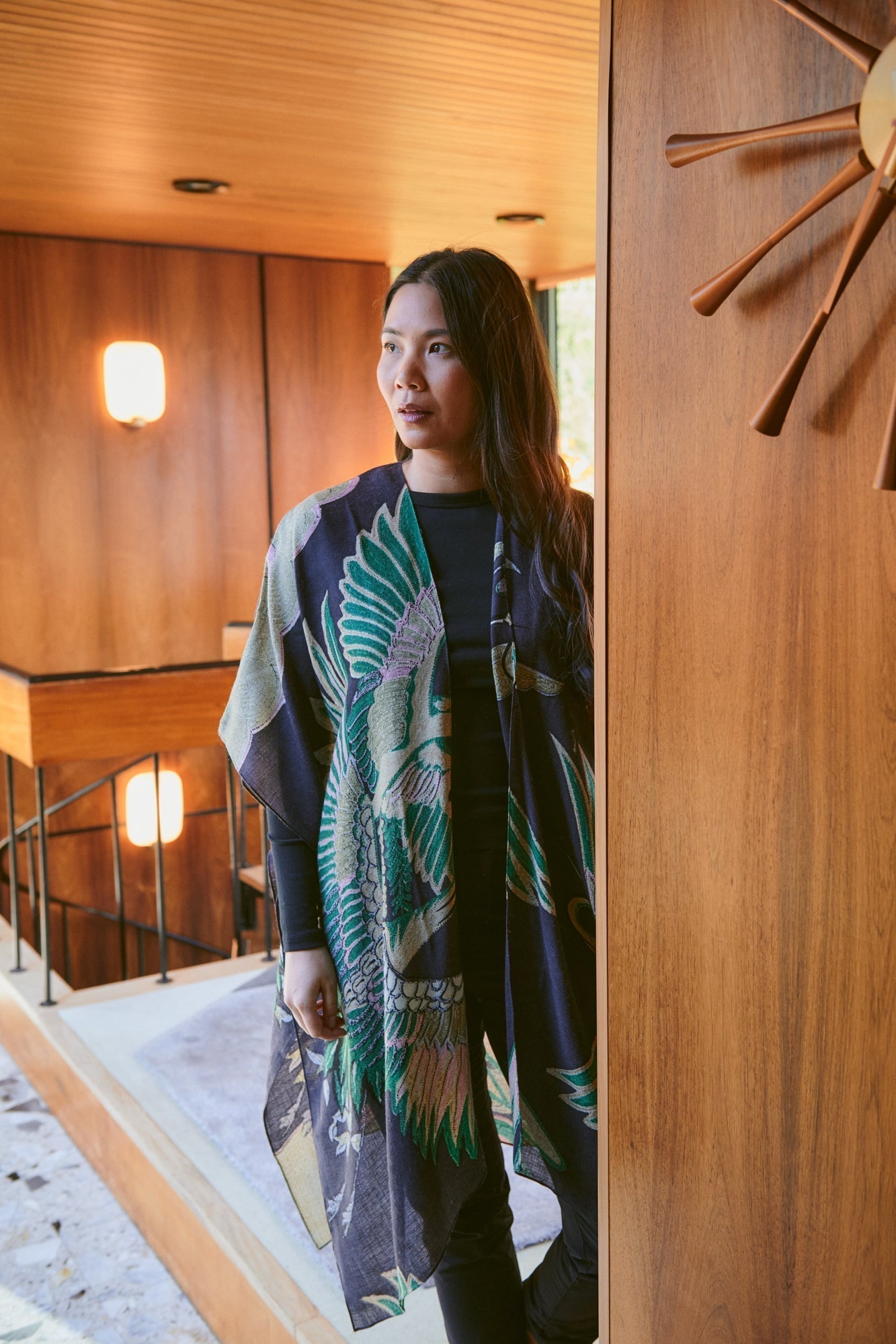 Woman wearing a patterned throwover in an indoor setting with wooden walls and a staircase.