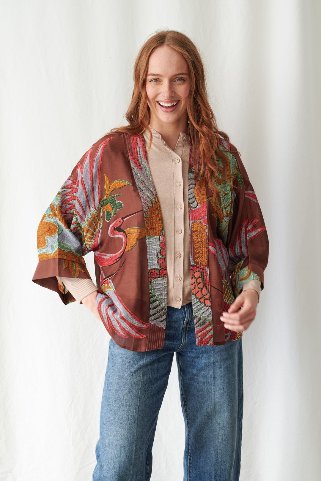 Woman wearing a colorful patterned jacket over a beige shirt and blue jeans on a white background