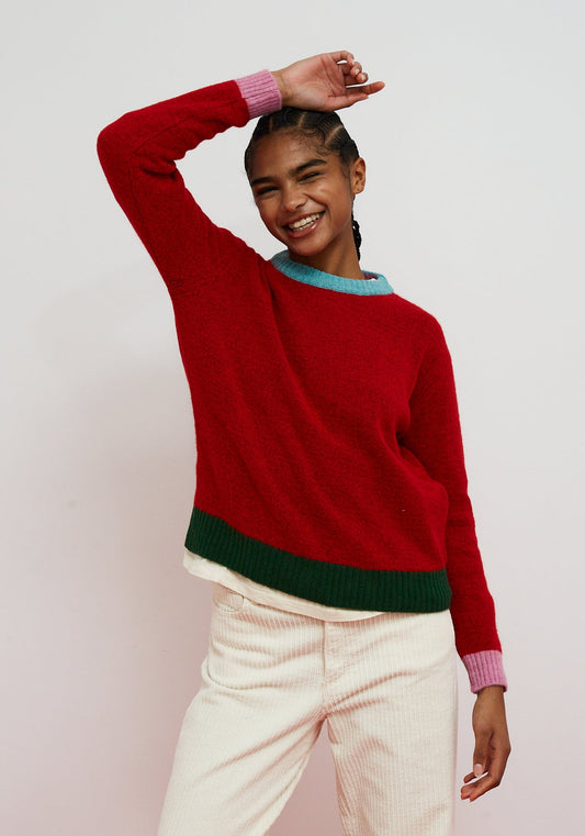 Person wearing a red sweater with green and blue accents on a light pink background