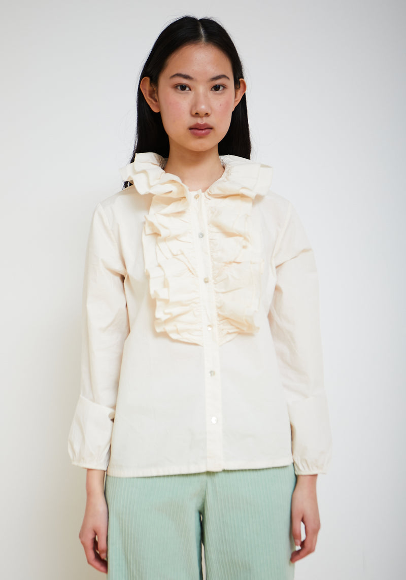 Woman wearing a cream-colored blouse with ruffled details on a white background