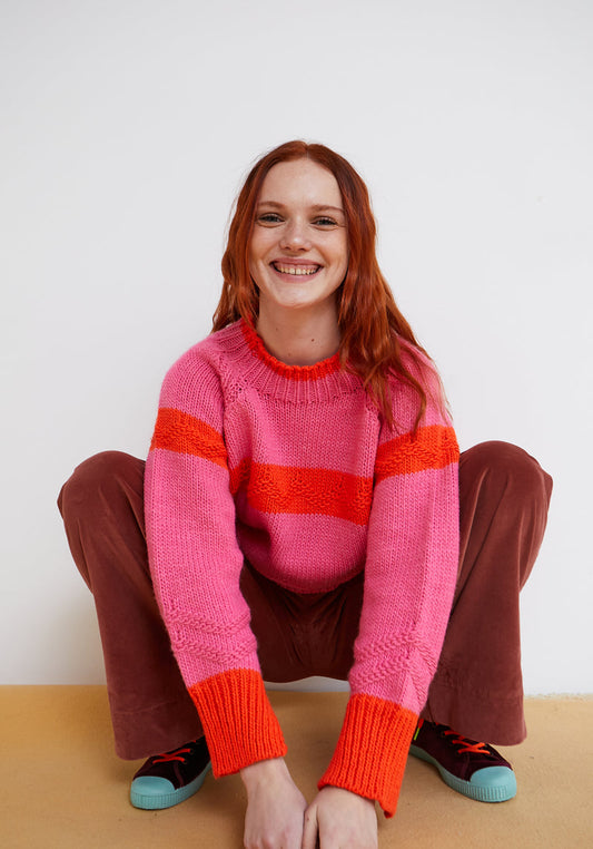 Person wearing a pink sweater with red stripes sitting on a wooden floor.