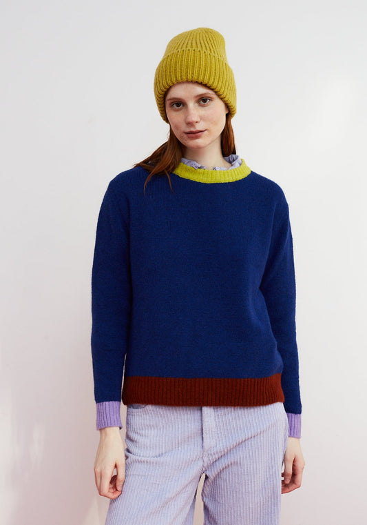 Dr Bloom Jersey Moss Blue. Person wearing a blue sweater with a yellow beanie and purple accents against a white background