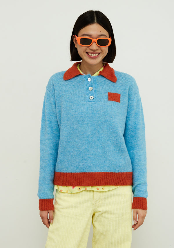 Dr Bloom Jersey Poppy Blue. Person wearing a blue sweater with red collar and cuffs, yellow pants, and orange sunglasses against a white background