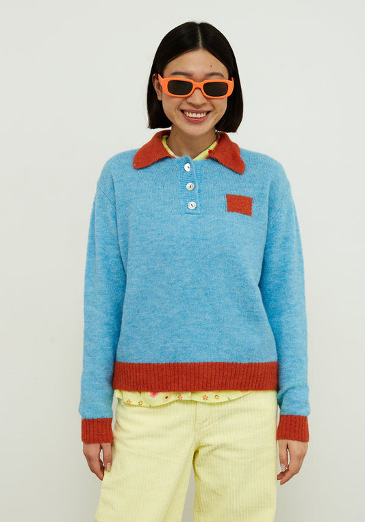 Dr Bloom Jersey Poppy Blue. Person wearing a blue sweater with red collar and cuffs, yellow pants, and orange sunglasses against a white background