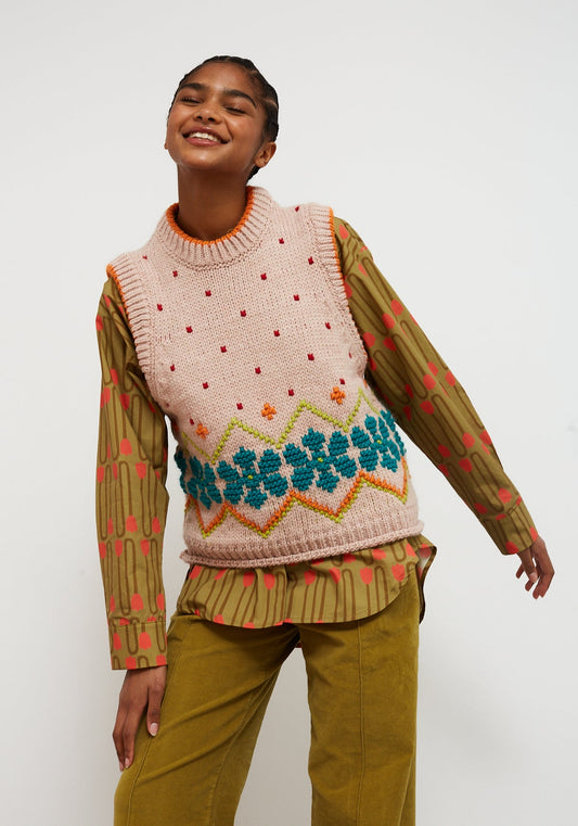 Dr Bloom Jumpy Nude Vest. Person wearing a patterned sweater vest over a long-sleeve shirt with a white background