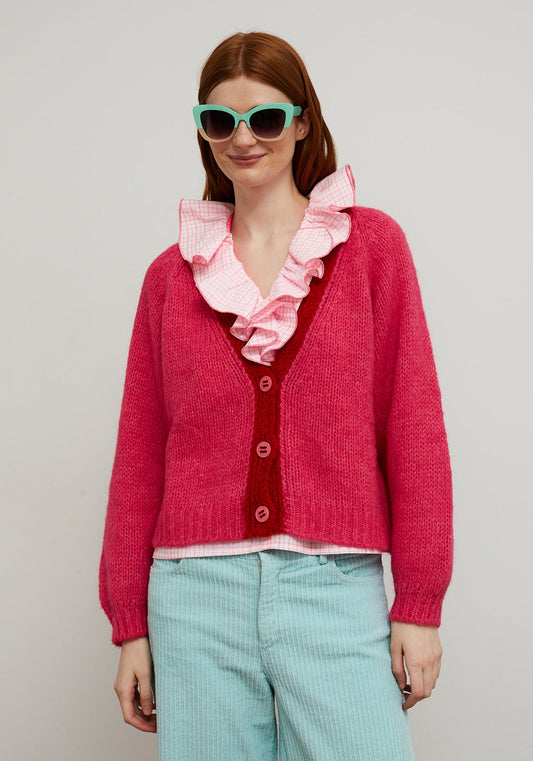 Dr Bloom Pink Cocoon Cardigan. Woman wearing a pink cardigan with a ruffled collar, red shirt, and light blue pants against a plain background.