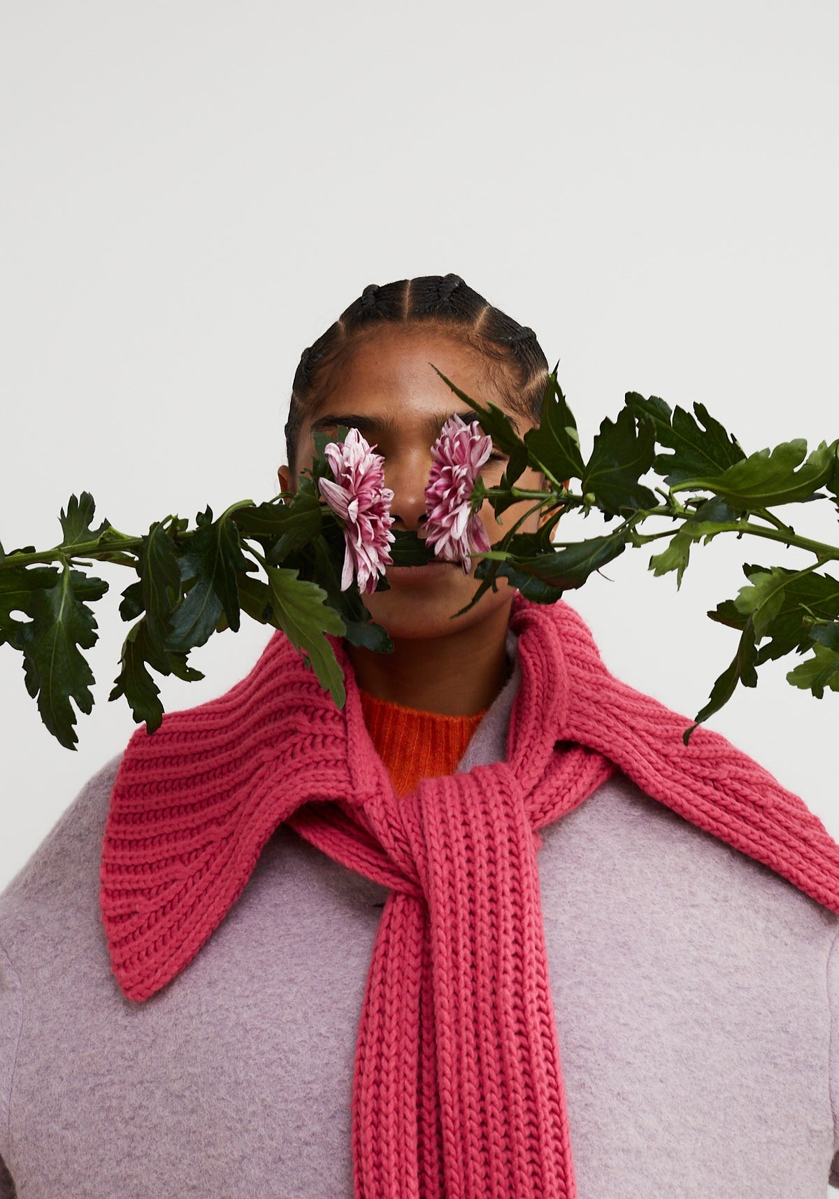 Dr Bloom Spark Pink Collar-Scarf. Person wearing a pink knitted scarf with flowers and leaves in front of their face on a light background