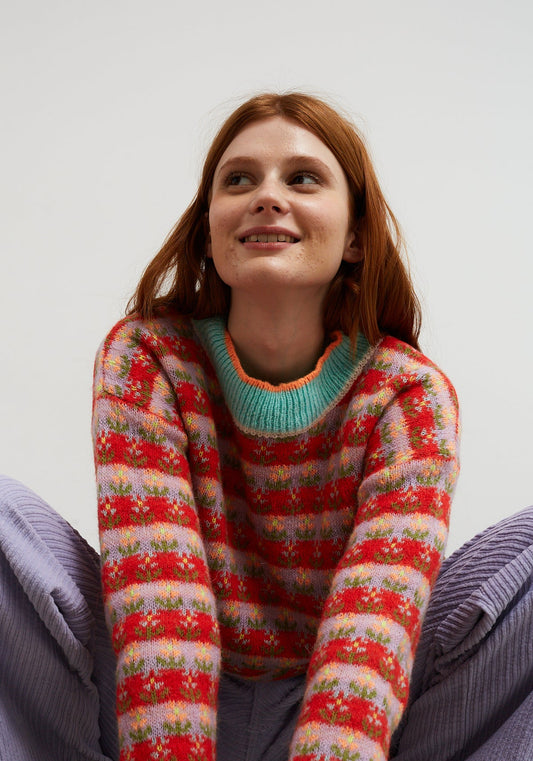 Dr Bloom Sweater Blossom Red. Woman wearing a colourful sweater against a plain background