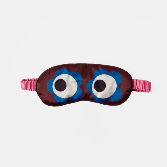 A sleep mask with a dark brown satin body, featuring two large blue flower-shaped eyes with white and black centers, and a pink elastic strap, shown against a light gray background.