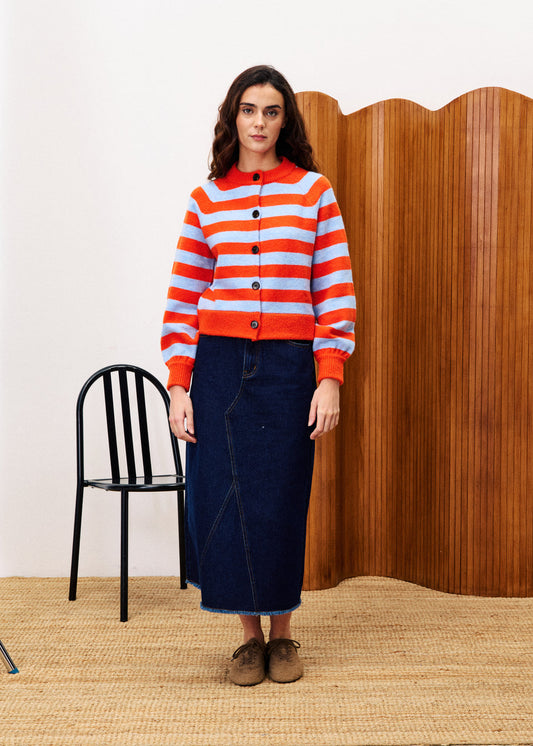 FRNCH MORAND Red Cardigan. Woman wearing a red and orange striped sweater with a wooden wall and black chair in the background