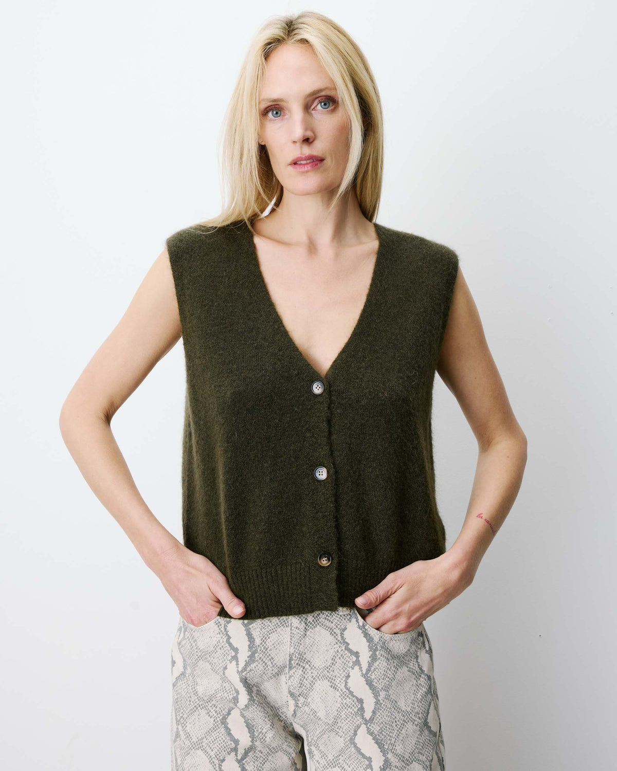Woman wearing a khaki vest against a plain background