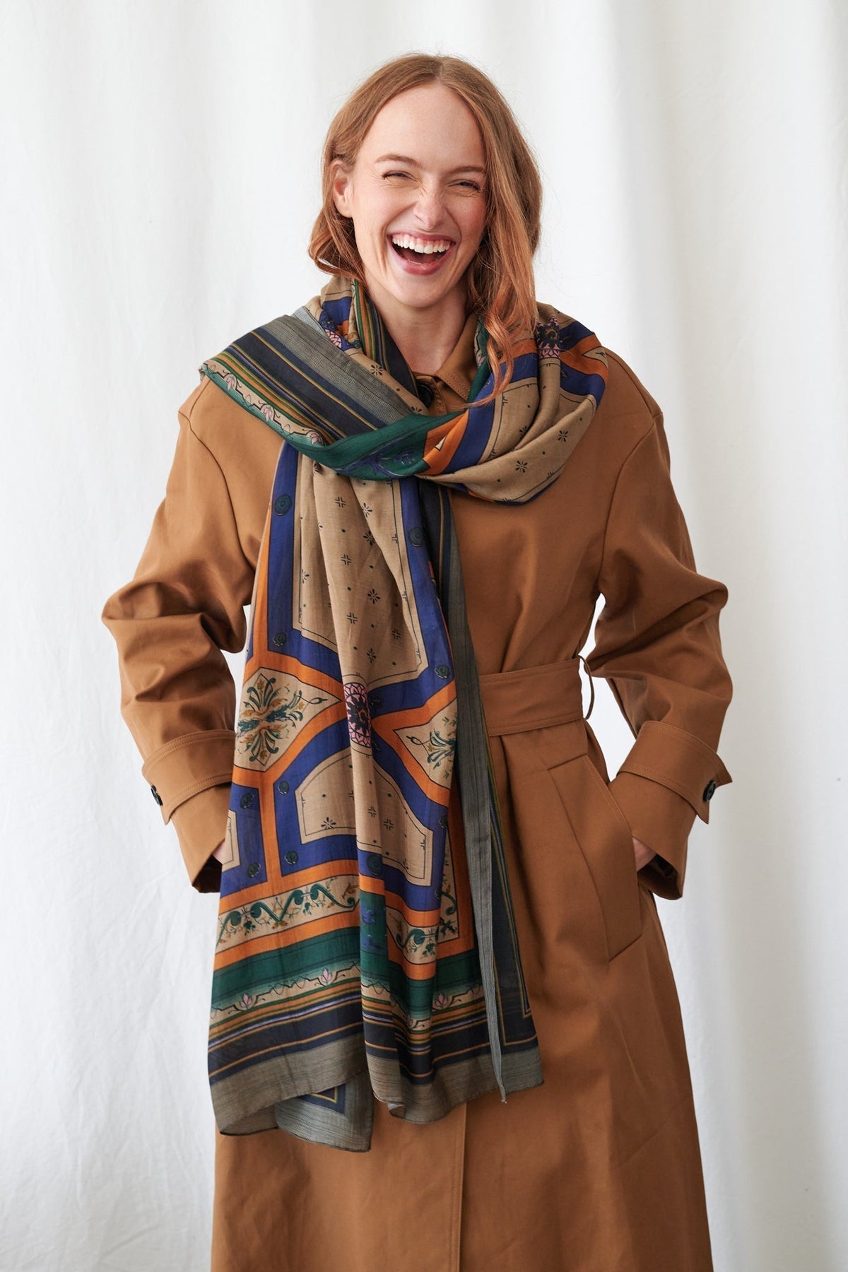 Woman wearing a brown coat and colorful scarf against a white background