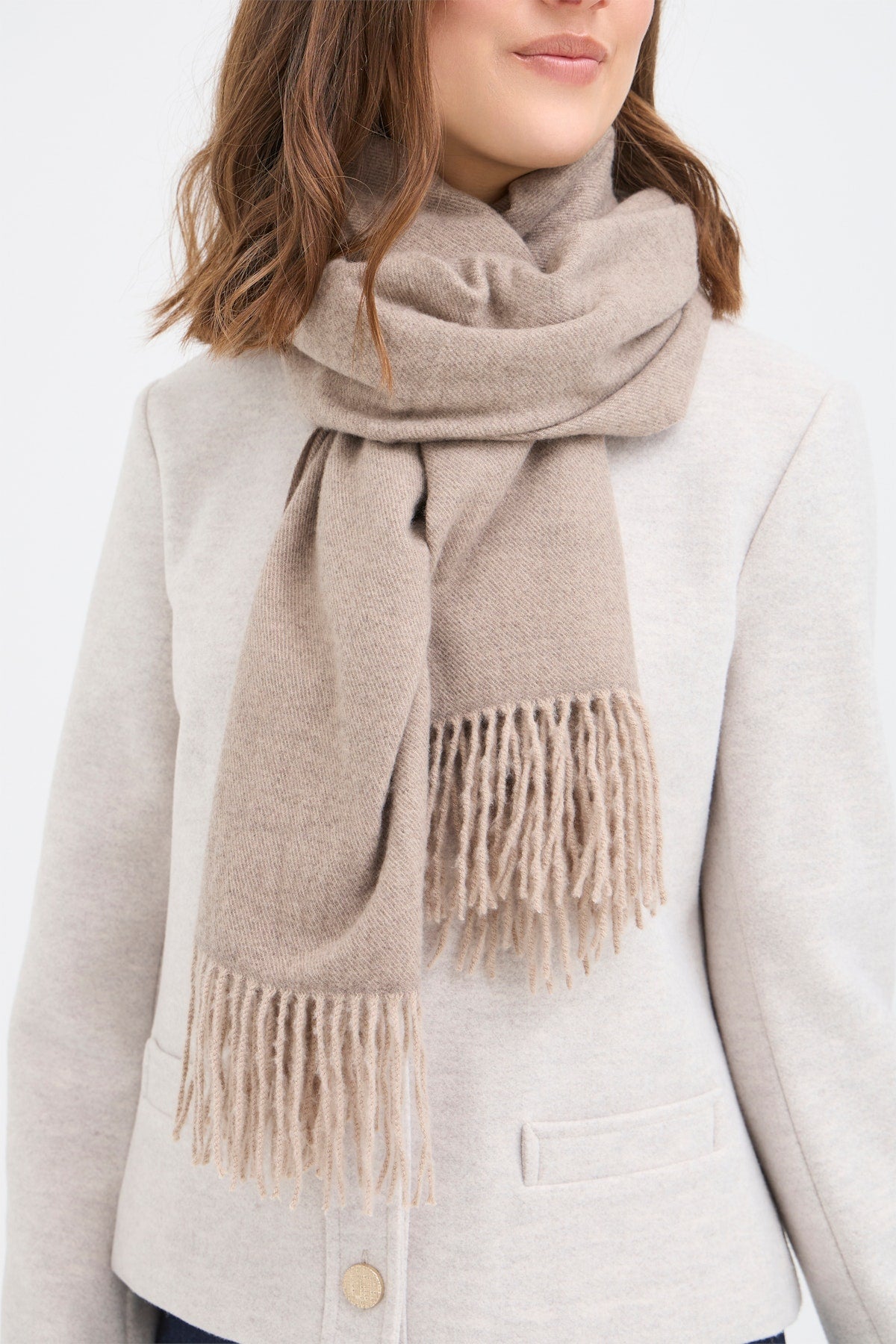 Fransa Pasmira Scarf in Desert Sand. Person wearing a beige scarf with fringes on a plain background