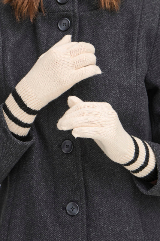 Fransa Stripy Gloves in Whisper White Mix. Person wearing a dark coat with white gloves and black stripes on a plain background