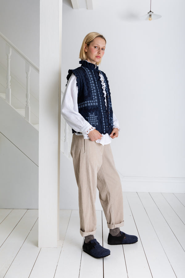 Person wearing a dark denim Bonte London Gwen Gilet vest over a white shirt with beige pants in a minimalistic setting.