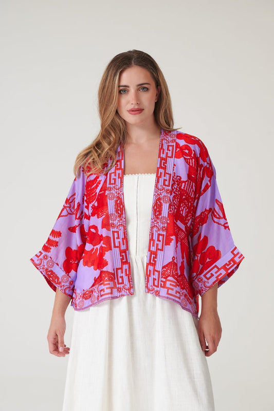 Woman wearing a red and purple patterned kimono over a white dress on a plain background