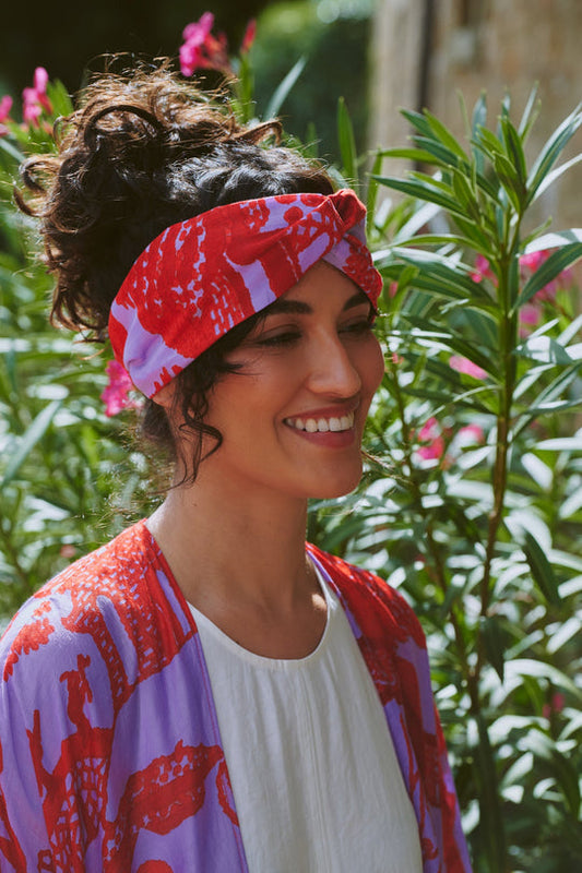 Woman wearing a red and purple headscarf and patterned outfit in a garden setting