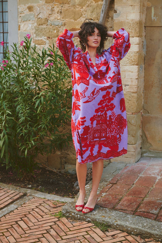 Woman wearing a red and white patterned dress standing outdoors near a stone building.