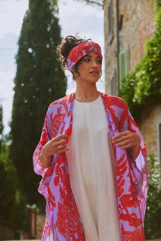 Woman wearing a red and purple patterned kimono-style garment outdoors.
