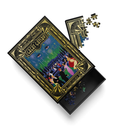 An Art Deco style jigsaw puzzle box shown open on a white background, with the lid featuring a gold-bordered illustration of a dancing couple and the text 'GREAT GATSBY'. Several loose puzzle pieces are scattered beside and inside the box.