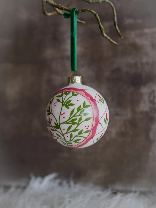 Decorative Christmas ball ornament with floral design hanging on a branch.