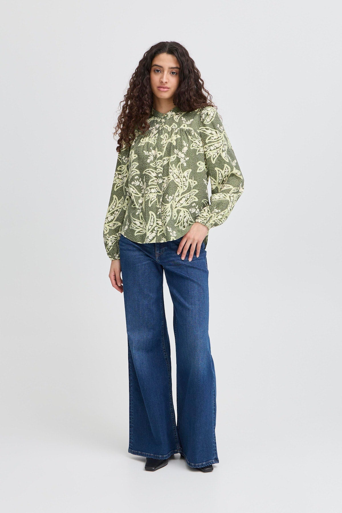 ICHI Finola Shirt in Vintage Floral. Woman wearing a green floral blouse and blue jeans on a white background