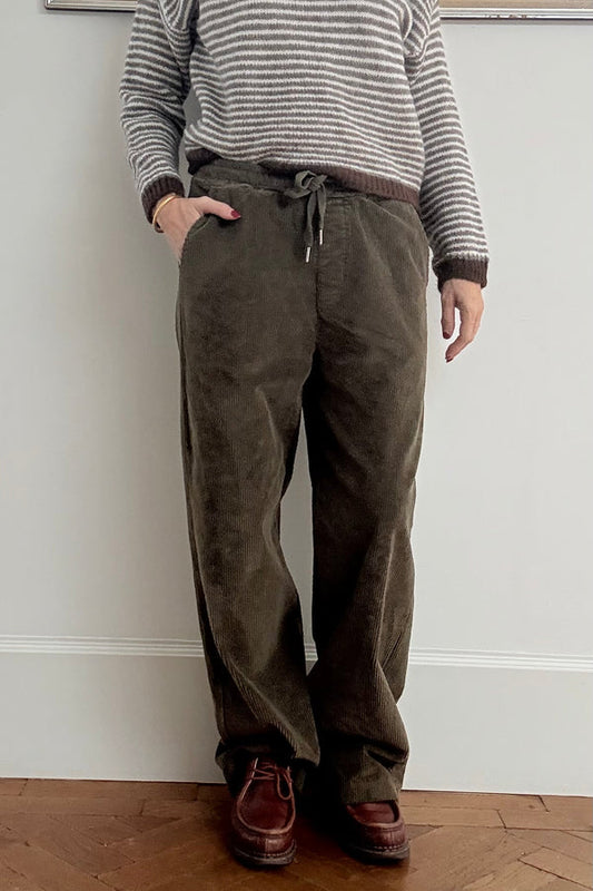 Person wearing a striped sweater and corduroy pants standing against a plain wall.