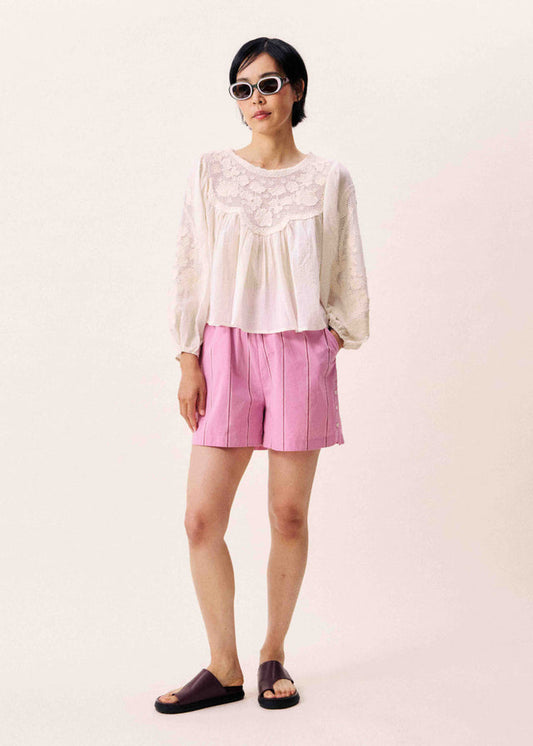 Woman wearing a white lace top and pink shorts on a plain background