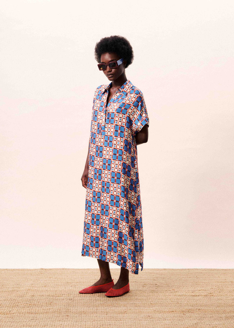 Woman wearing a patterned dress standing against a plain background