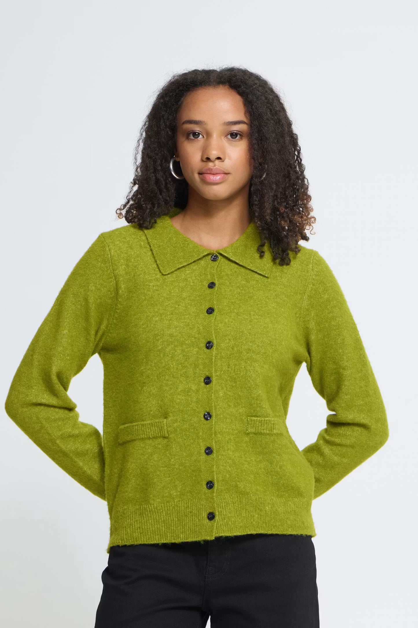 Woman wearing a green cardigan with a collar, pockets and black buttons on a white background